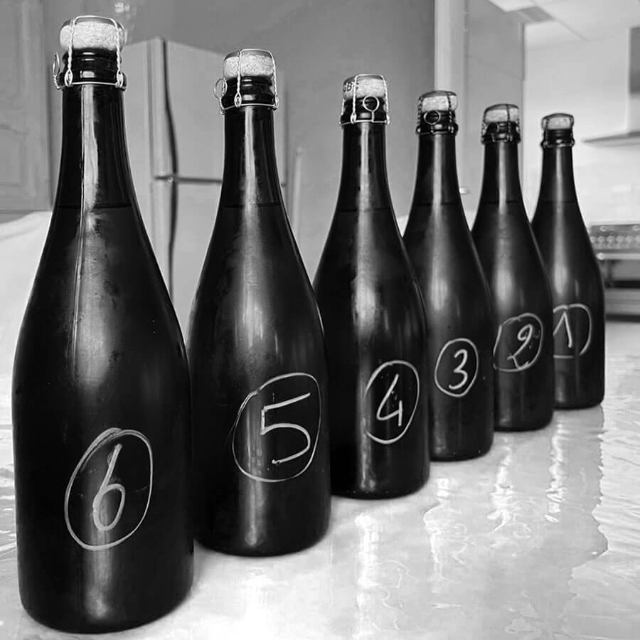 Six bouteilles de champagne noires numérotées de 6 à 1 alignées sur un comptoir, prêtes pour une dégustation à l’aveugle